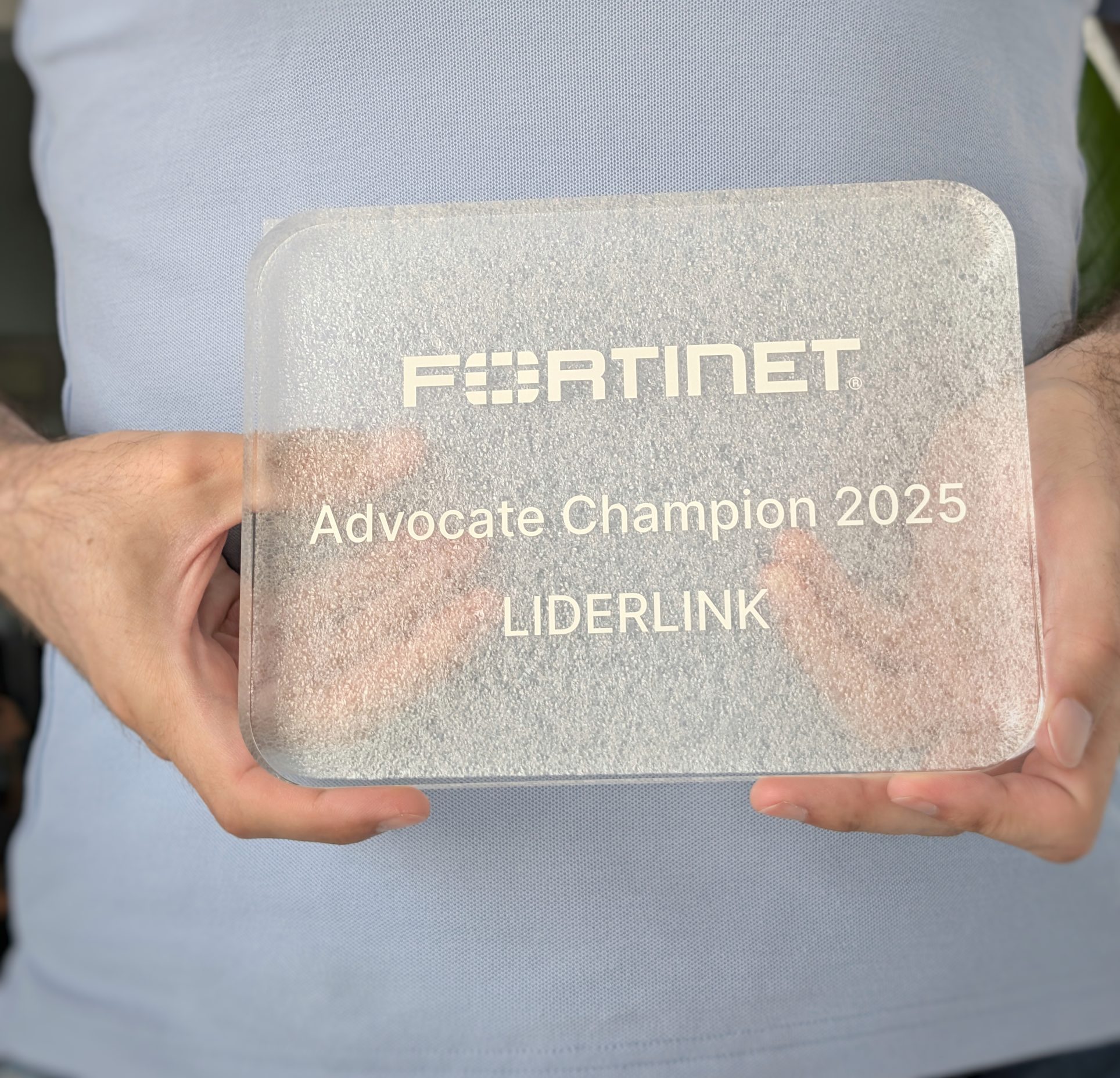 mãos a segurarem troféu Fortinet Advocate Champion 2025